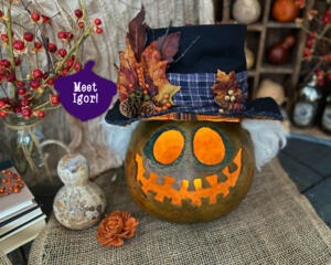 A Handmade spooky monster fall decoration with a whimsical toothy grin, a grungy top hat and candle. 